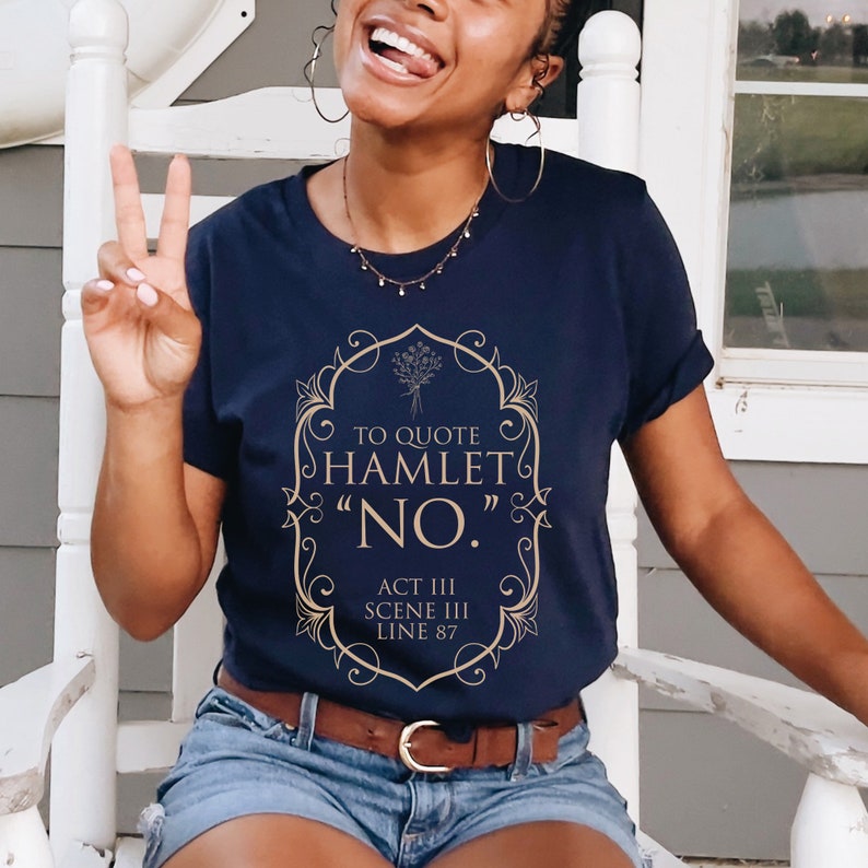 May include: A navy blue t-shirt with a gold graphic design featuring a quote from Hamlet: "To quote Hamlet "No." Act III Scene III Line 87"