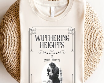 May include: A beige t-shirt with a black and white graphic of the book cover for "Wuthering Heights" by Emily Brontë. The graphic features a vintage-style illustration of a couple embracing.