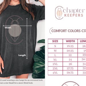 May include: Dark gray t-shirt with a graphic design and the text "chapter KEEPERS". The image includes a size chart with measurements in inches for width and length, ranging from size S to 4XL.