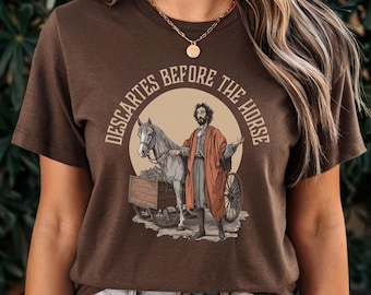Peut inclure: Un t-shirt marron avec un graphique d'un homme barbu avec un cheval tirant un chariot. Le texte sur le t-shirt est "Descartes Before The Horse."