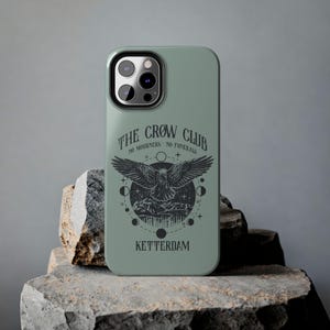 May include: A green phone case with a black crow design and the text "The Crow Club No Mourners No Funerals Ketterdam".
