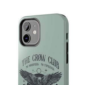 May include: A sage green phone case with a black crow graphic and the text "The Crow Club - No Mourners - No Funerals".