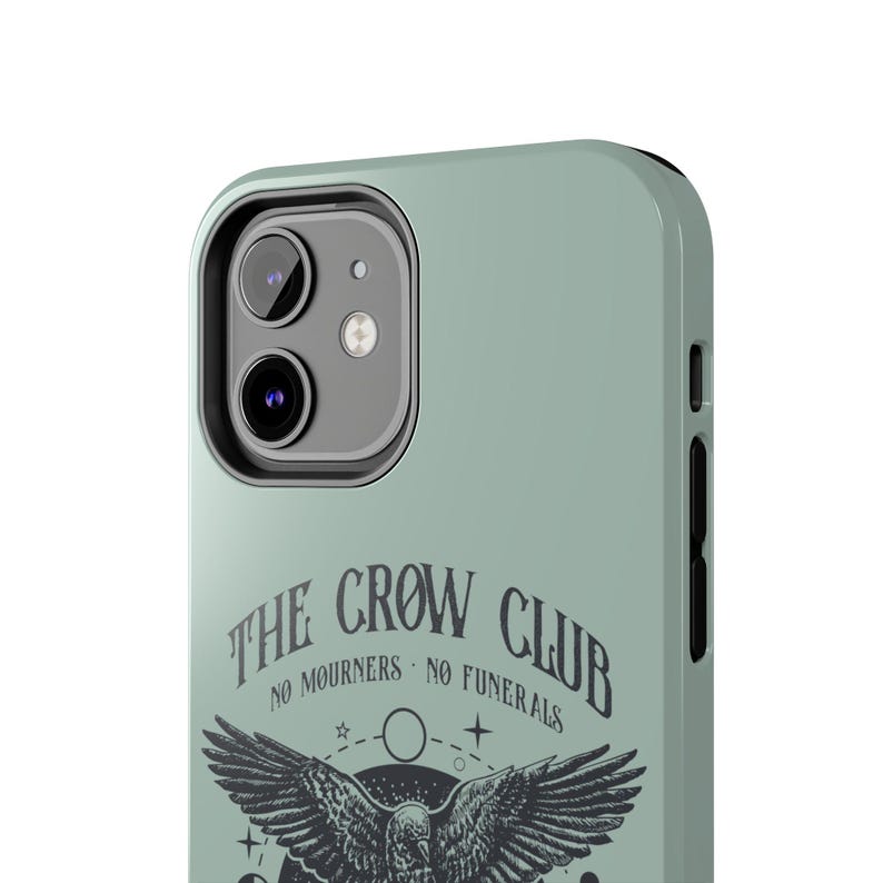 May include: A sage green phone case with a black crow graphic and the text "The Crow Club - No Mourners - No Funerals".