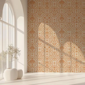 Puede incluir: Una pared beige con un patrón floral naranja repetido. El patrón presenta flores y hojas estilizadas dentro de marcos arqueados. La pared está en una habitación con una gran ventana arqueada y un jarrón blanco con una planta.