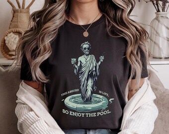 Peut inclure: Un t-shirt noir avec un graphique d'un homme dans une piscine tenant un verre. Le texte sur le t-shirt est "The absurd is life, so enjoy the pool."