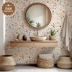May include: A bathroom scene with a round woven mirror, a stone sink, and a wooden floating shelf. The wall has a colorful terrazzo pattern. A woven basket and a potted plant are also visible.