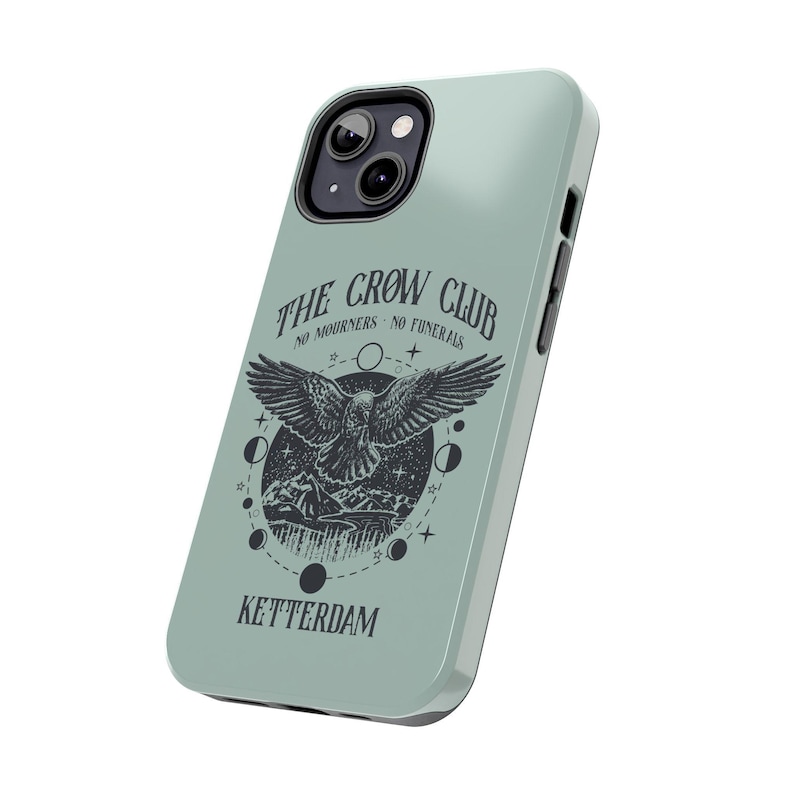 May include: A light blue phone case with a black and white illustration of a crow with the text "The Crow Club No Mourners No Funerals Ketterdam".