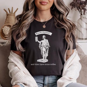 May include: A black t-shirt with a white graphic of a man holding a coffee cup. The text on the shirt reads "Know thyself... and then have some coffee."