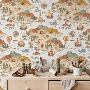 May include: A light-colored wallpaper featuring a repeating map pattern with mountains, forests, islands, sailing ships, hot air balloons, whales, and sea monsters. In front, a wooden dresser holds brass binoculars, glass jars, a compass, and a mug.