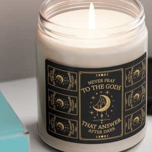May include: A black and gold candle with a label that reads "Never pray to the gods that answer after dark". The label features a crescent moon and stars.