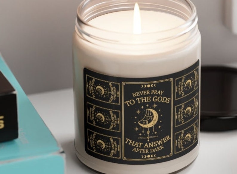 May include: A black and gold candle with a label that reads "Never pray to the gods that answer after dark". The label features a crescent moon and stars.