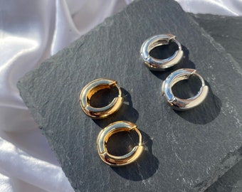 May include: Two pairs of hoop earrings, one pair is gold and the other is silver. The earrings are on a black slate surface.