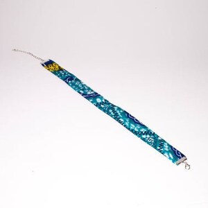 Puede incluir: Un collar gargantilla de tela con estampado azul y amarillo con extremos de cadena plateados.