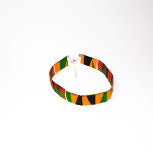 Puede incluir: Un collar gargantilla de tela colorido con un patr&oacute;n verde, amarillo, rojo y negro. El collar tiene un cierre plateado.