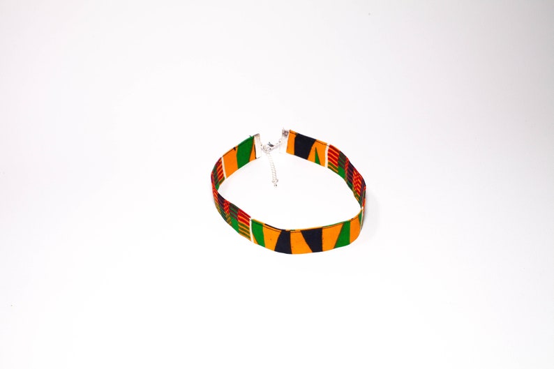 Puede incluir: Un collar gargantilla de tela colorido con un patr&oacute;n verde, amarillo, rojo y negro. El collar tiene un cierre plateado.