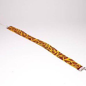 Puede incluir: Un collar gargantilla de tela con estampado amarillo y rojo con cierres plateados.