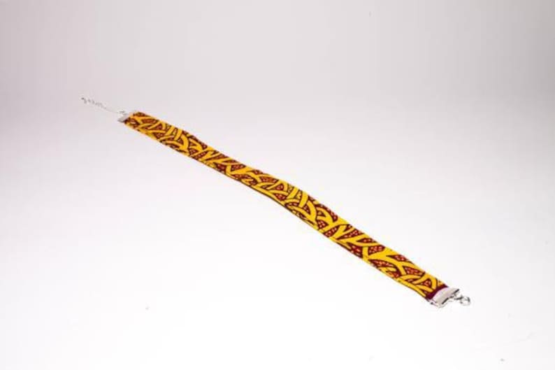 Puede incluir: Un collar gargantilla de tela con estampado amarillo y rojo con cierres plateados.