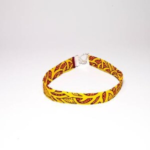 Puede incluir: Un collar gargantilla de tela con estampado amarillo y rojo con cierre plateado.