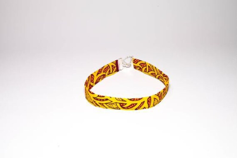 Puede incluir: Un collar gargantilla de tela con estampado amarillo y rojo con cierre plateado.