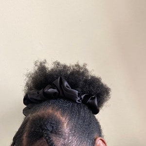 May include: A black satin scrunchie holding a person's afro hair in a high ponytail.