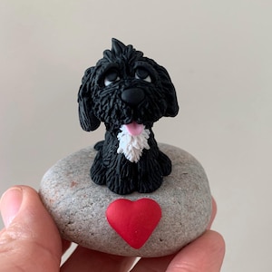 May include: A black and white dog figurine with a red heart on a grey stone. The dog is sitting up with its tongue sticking out.