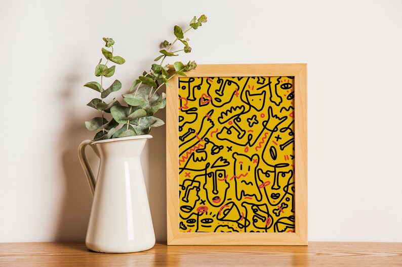 May include: A framed print with a yellow background and black line drawings of abstract faces and shapes. The print is in a wooden frame.