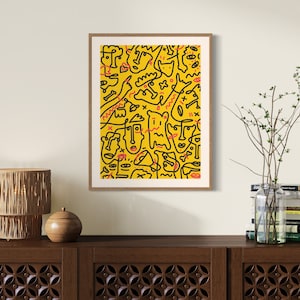 May include: A framed print with a yellow background and black and red abstract line drawings. The print is hanging on a white wall above a wooden cabinet.