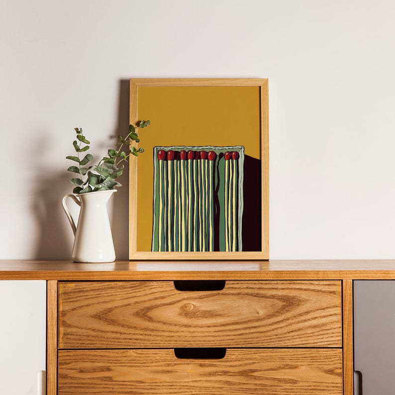 May include: A framed illustration of a box of matches with red heads on a yellow background.