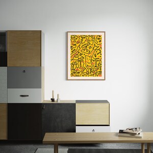 May include: A framed print of a yellow and black abstract design with red accents. The design features a variety of shapes and lines, including faces and figures.
