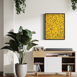 May include: A black framed print of a yellow background with black line drawings of faces and abstract shapes. The print is hanging on a white wall above a wooden shelf with books and a record player.