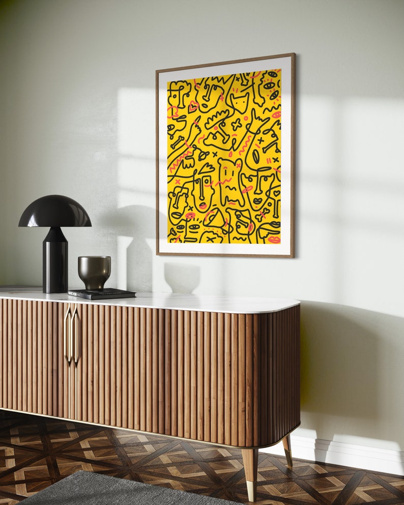 May include: A framed print with a yellow background and black line drawings of faces, figures, and abstract shapes. The artwork has a modern and abstract style.