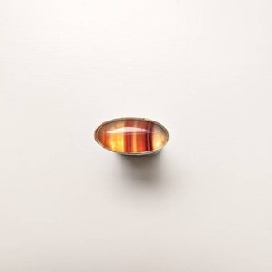 May include: A ring featuring a red, orange and yellow agate stone set in a silver band.
