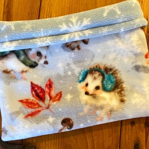 May include: A blue fleece hedgehog-themed pet bed with a white snowflake pattern. The bed is folded in half and has a white fleece lining.