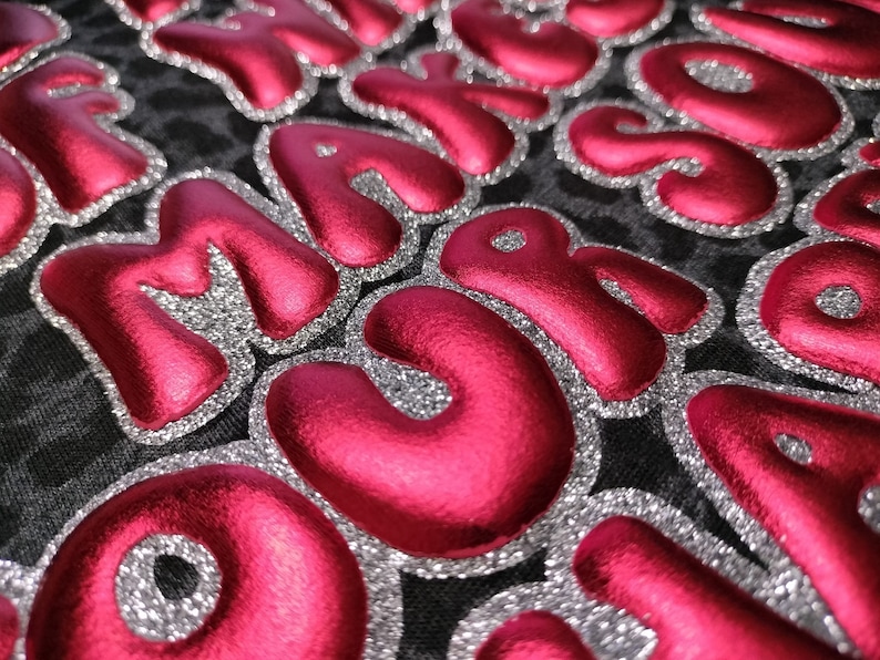 May include: Close-up of a fabric with the word "MAYO" spelled out in large, puffy, pink letters with silver glitter trim.