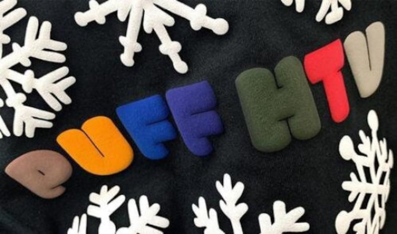 May include: A black sweatshirt with the words "PUFF HTV" in colorful, puffy letters. The letters are in different colors, including orange, blue, green, and red. The sweatshirt also has a white snowflake pattern.