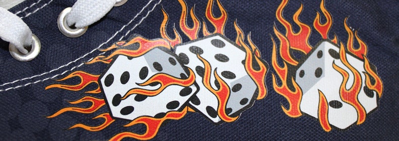 May include: A pair of white dice with black dots are set against a dark blue background. The dice are surrounded by orange and red flames.