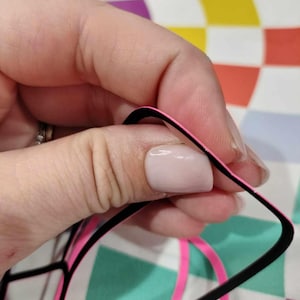 Może przedstawiać: Czarne i r&oacute;żowe okulary z grubą czarną oprawką i r&oacute;żowym wykończeniem. Okulary są trzymane przez rękę.