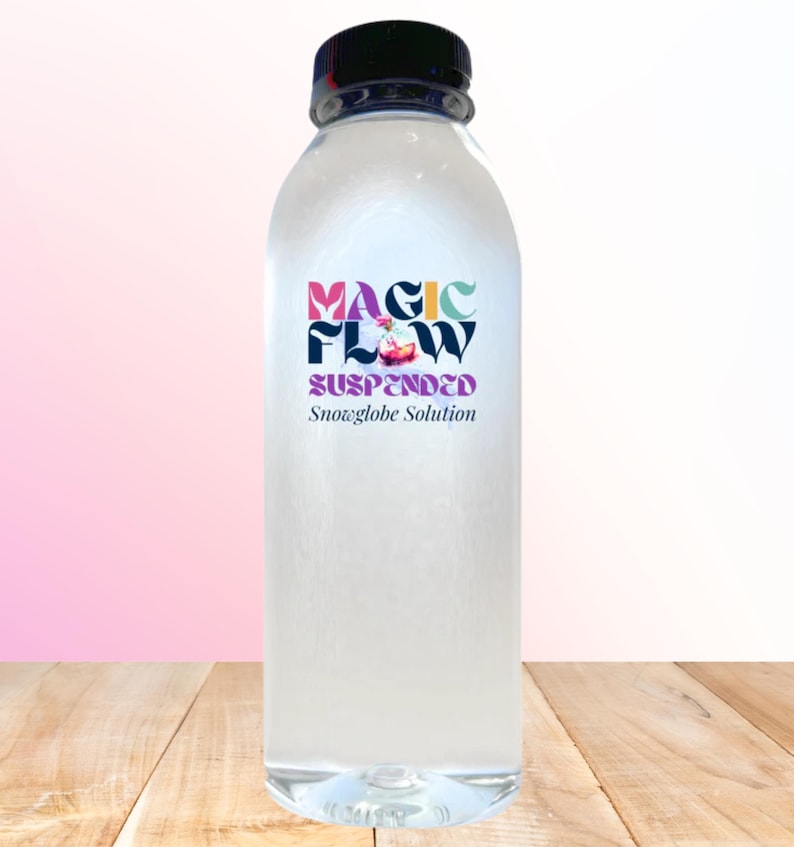 May include: A clear plastic bottle with a black cap, filled with a liquid. The bottle has a colorful label that reads "MAGIC FLOW SUSPENDED Snowglobe Solution". The bottle is sitting on a wooden surface.