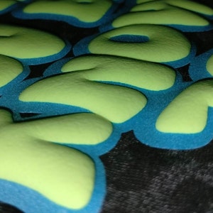 May include: Close-up of a green and blue fabric with the word "YOU" spelled out in raised letters.