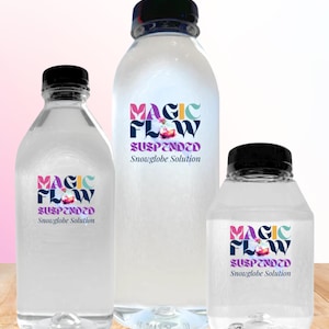 Può includere: Tre bottiglie di plastica trasparente con tappi neri, ciascuna etichettata "MAGIC FLOW Suspended Snowglobe Solution". Le etichette presentano testo colorato e una piccola grafica. Le bottiglie variano in dimensioni.