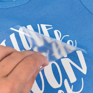 Puede incluir: Un body de beb&eacute; azul con el texto "Me encanta la luna pero..." y el resto del texto est&aacute; oculto por una l&aacute;mina de pl&aacute;stico transparente.