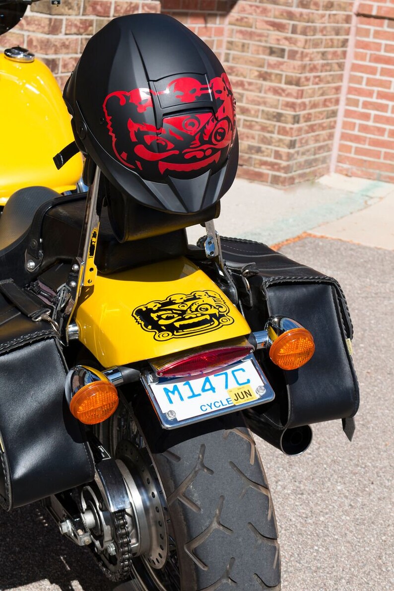 May include: A yellow motorcycle with black leather saddlebags and a black helmet with a red and black graphic. The motorcycle has a license plate that reads "M147C CYCLE JUN".