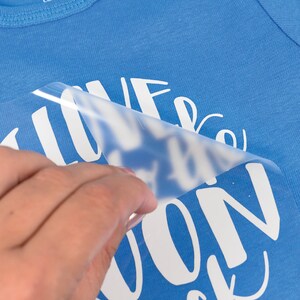 May include: A blue baby onesie with the text "I love the moon but..." and the rest of the text is obscured by a clear plastic sheet.