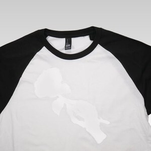 May include: White baseball tee with black sleeves and a white silhouette of a rose on the front.