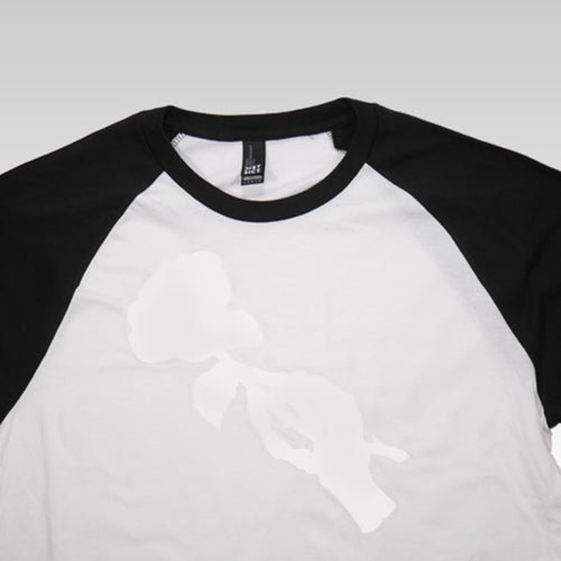 May include: White baseball tee with black sleeves and a white silhouette of a rose on the front.
