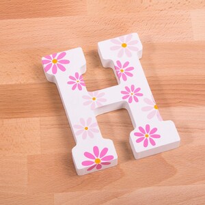 May include: White wooden letter H with pink and yellow flowers painted on it.