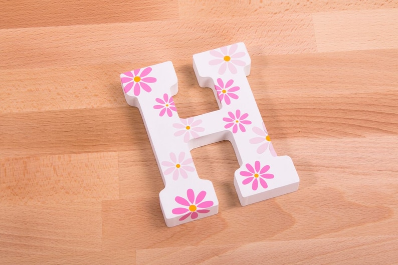 May include: White wooden letter H with pink and yellow flowers painted on it.