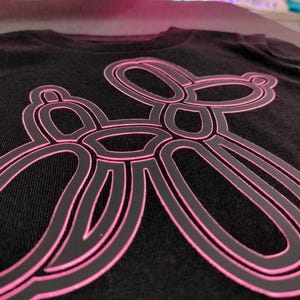 Może przedstawiać: Czarny t-shirt z r&oacute;żowym konturem zwierzęcia z balonu w kształcie psa.