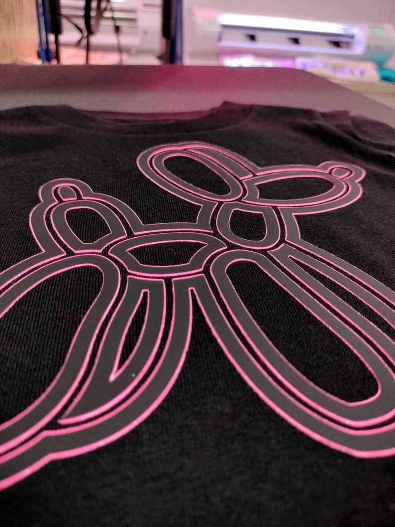 Może przedstawiać: Czarny t-shirt z r&oacute;żowym konturem zwierzęcia z balonu w kształcie psa.