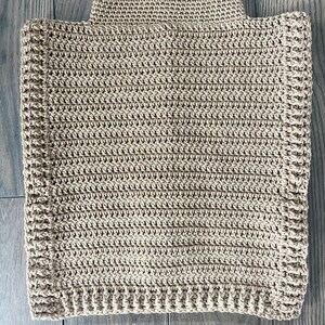 K&ouml;nnte beinhalten: Ein beigefarbener, handgeh&auml;kelter Poncho mit Rollkragen. Der Poncho hat eine rechteckige Form und ein strukturiertes Stichmuster. Die neutrale Farbe und das schlichte Design machen ihn zu einem vielseitigen Kleidungsst&uuml;ck zum &Uuml;berziehen.